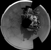 A mosaic of 20 full-resolution images taken from Curiosity's left Navcam on the second day after landing shows the rover, with a dirty deck, sitting on a gravelly plain, surrounded by mountains.