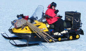 Amy eats lunch sitting proud and tall on her ski-doo; screw the wind.
